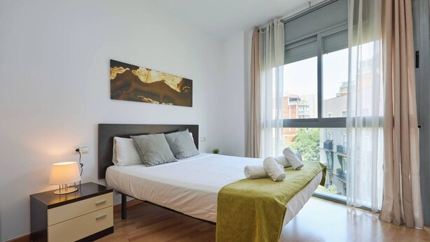 A modern bedroom with a bed, bedside table, and a window with curtains.