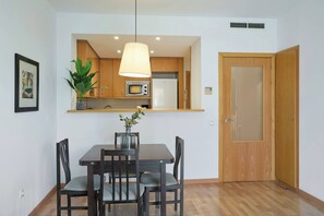 Cocina pequeña con armarios de madera, microondas y refrigerador. Hay una mesa de comedor con sillas y una lámpara colgante encima.