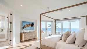 Ein geräumiges Schlafzimmer mit einem großen Bett, einer Holzkommode und Meerblick durch große Fenster.