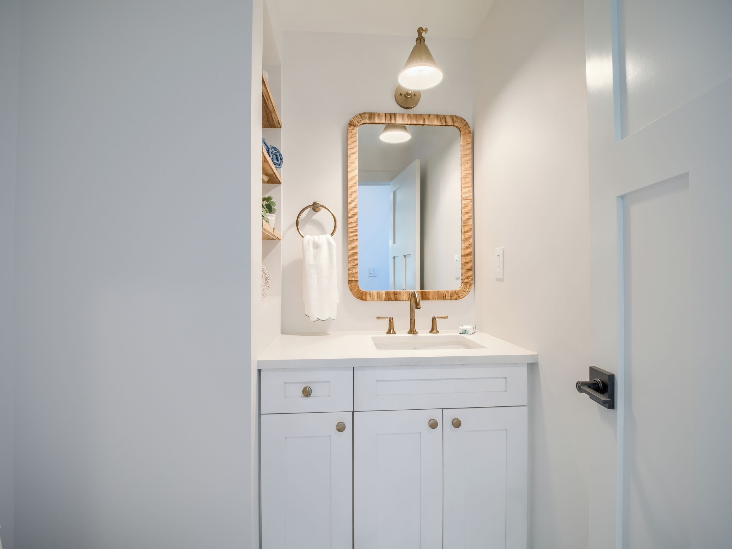 Une salle de bain avec un meuble-lavabo blanc, un miroir avec un cadre en bois et une serviette accrochée au mur.