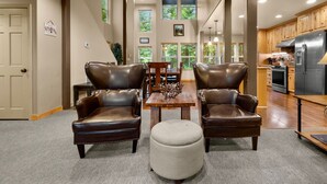 A spacious living room with leather armchairs, a wooden dining table, and a large window providing a view of the outdoors. - Evergreen House in heart Government Camp (Government Camp)