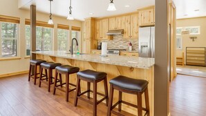 A modern kitchen with wooden cabinets, a stainless steel refrigerator, and a bar area with stools. - Evergreen House in heart Government Camp (Government Camp)
