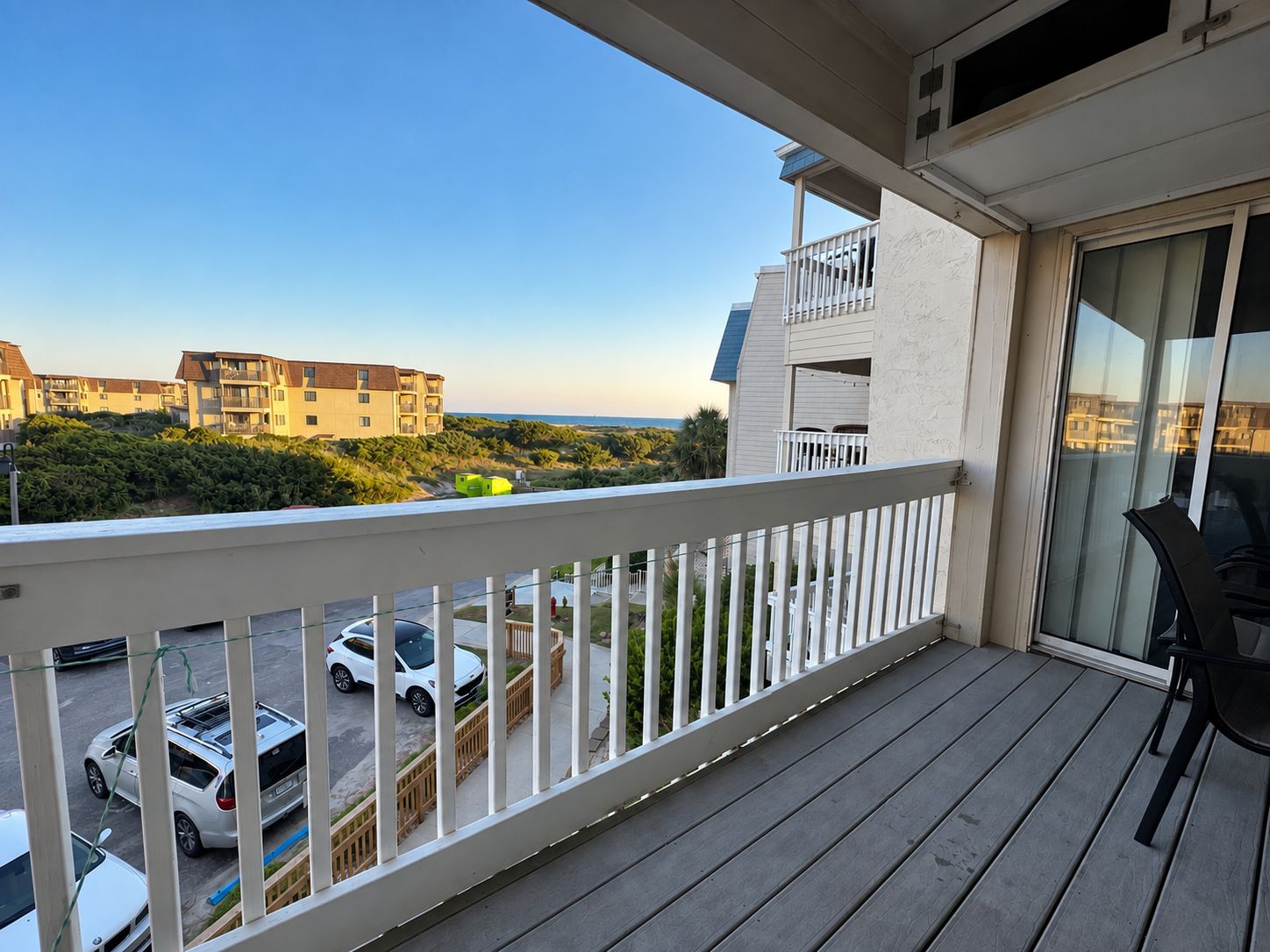 A balcony with a view of a road and buildings, a glass door, and a chair.