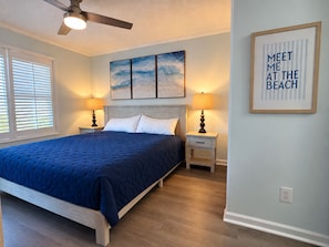 Une chambre à coucher avec un lit, deux tables de chevet, un ventilateur de plafond et des œuvres d’art accrochées au mur.