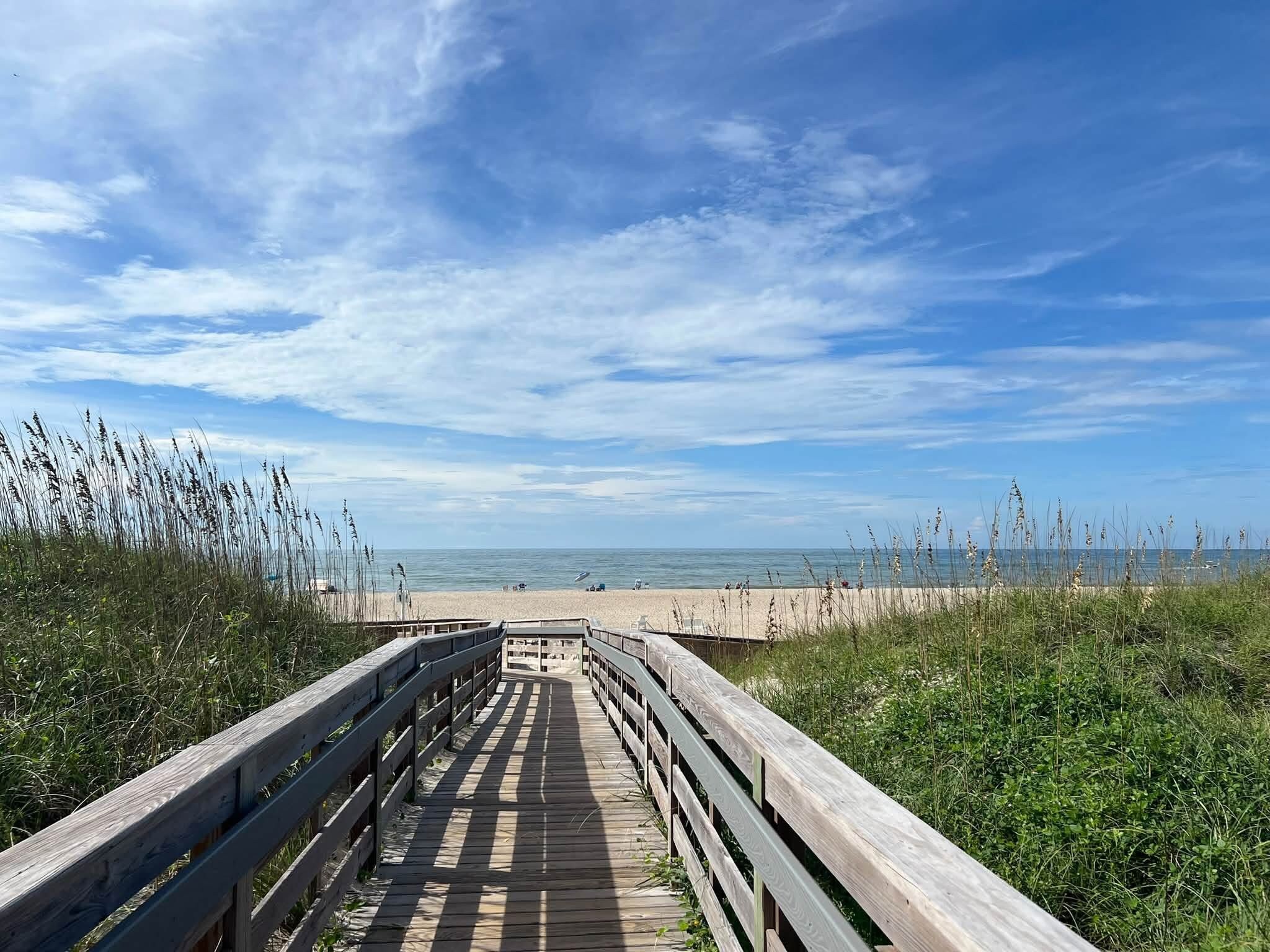 A wooden boardwalk leading to a beach with a clear sky.