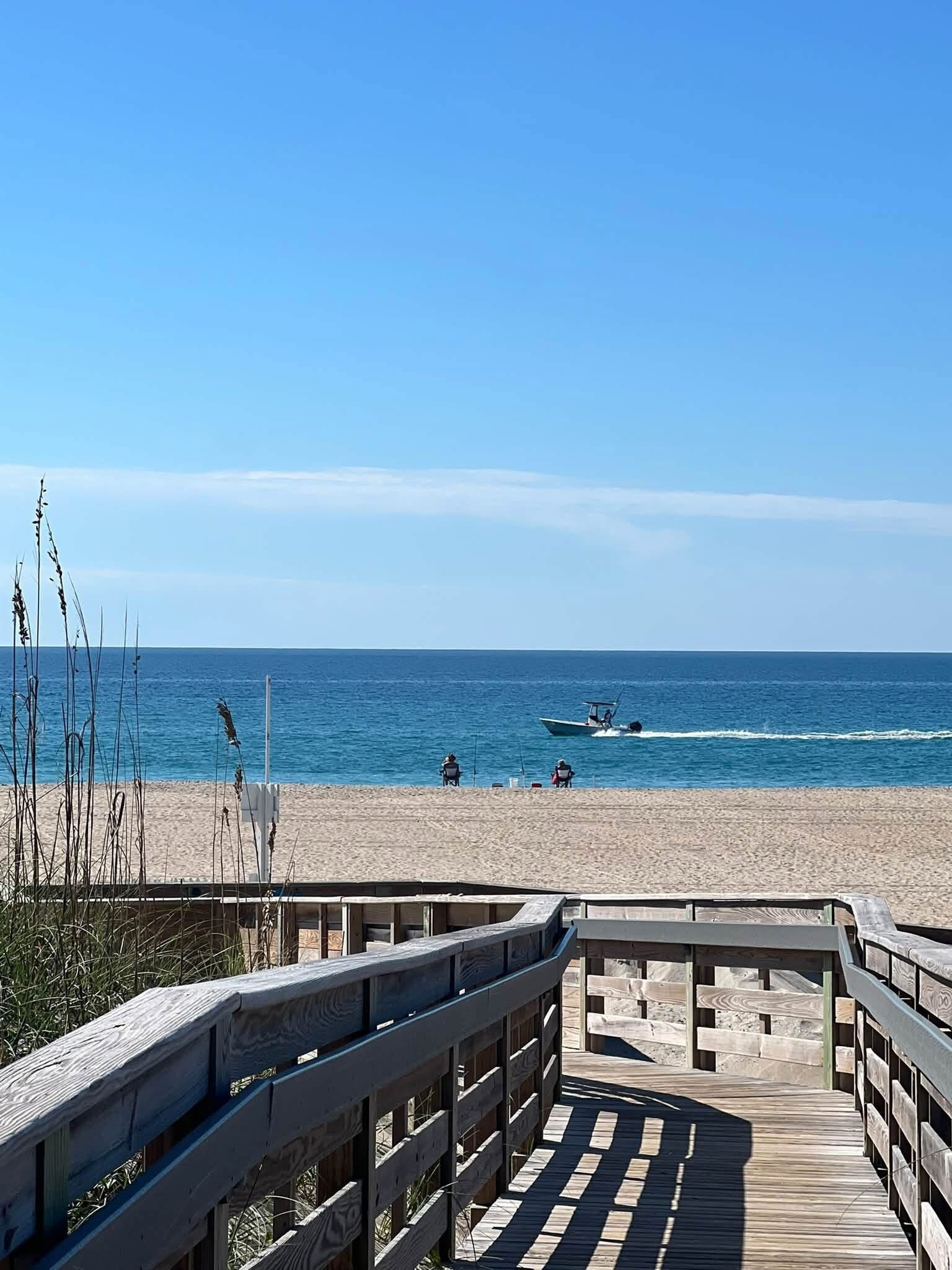 Pasarela de madera que conduce a una playa con vista despejada al océano y un barco a lo lejos.