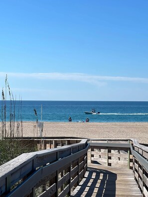 A wooden boardwalk leading to a beach with a clear view of the ocean and a boat in the distance.