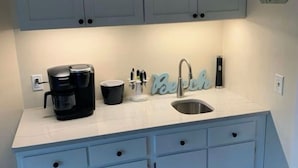 A kitchen with light blue cabinets, a white countertop, a coffee maker, a sink, and a decorative sign.