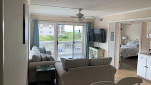A living room with a sofa, a television, and a balcony with a view of buildings.