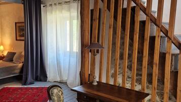 Ein Zimmer mit einer Holztreppe, einem Schreibtisch aus Holz, einem gemusterten Sessel, einem roten Teppich und einem Bett mit Lampe.