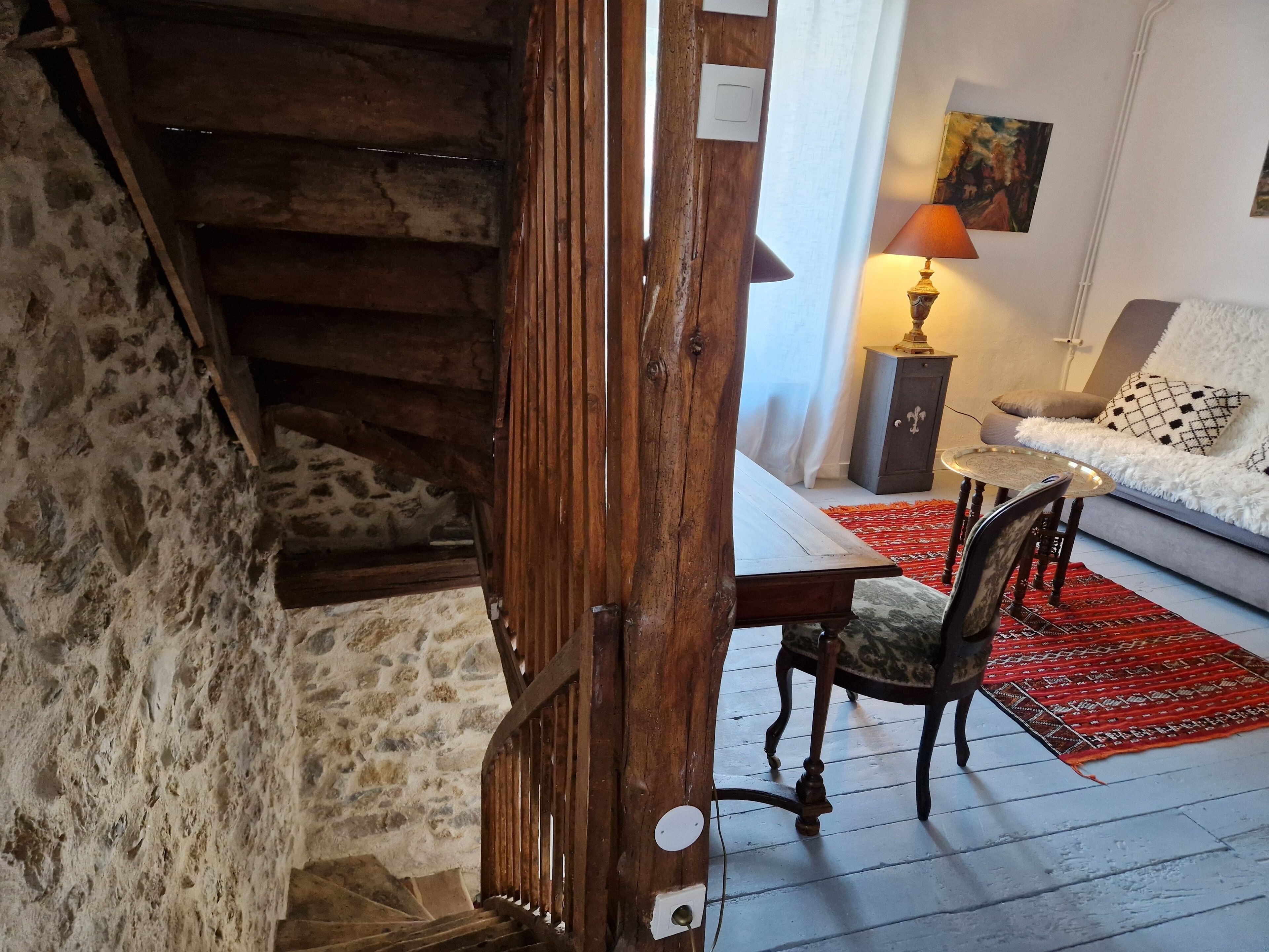 Una scala rustica con pareti in pietra, un tavolo di legno con sedie, un tappeto decorato e un divano con cuscini.