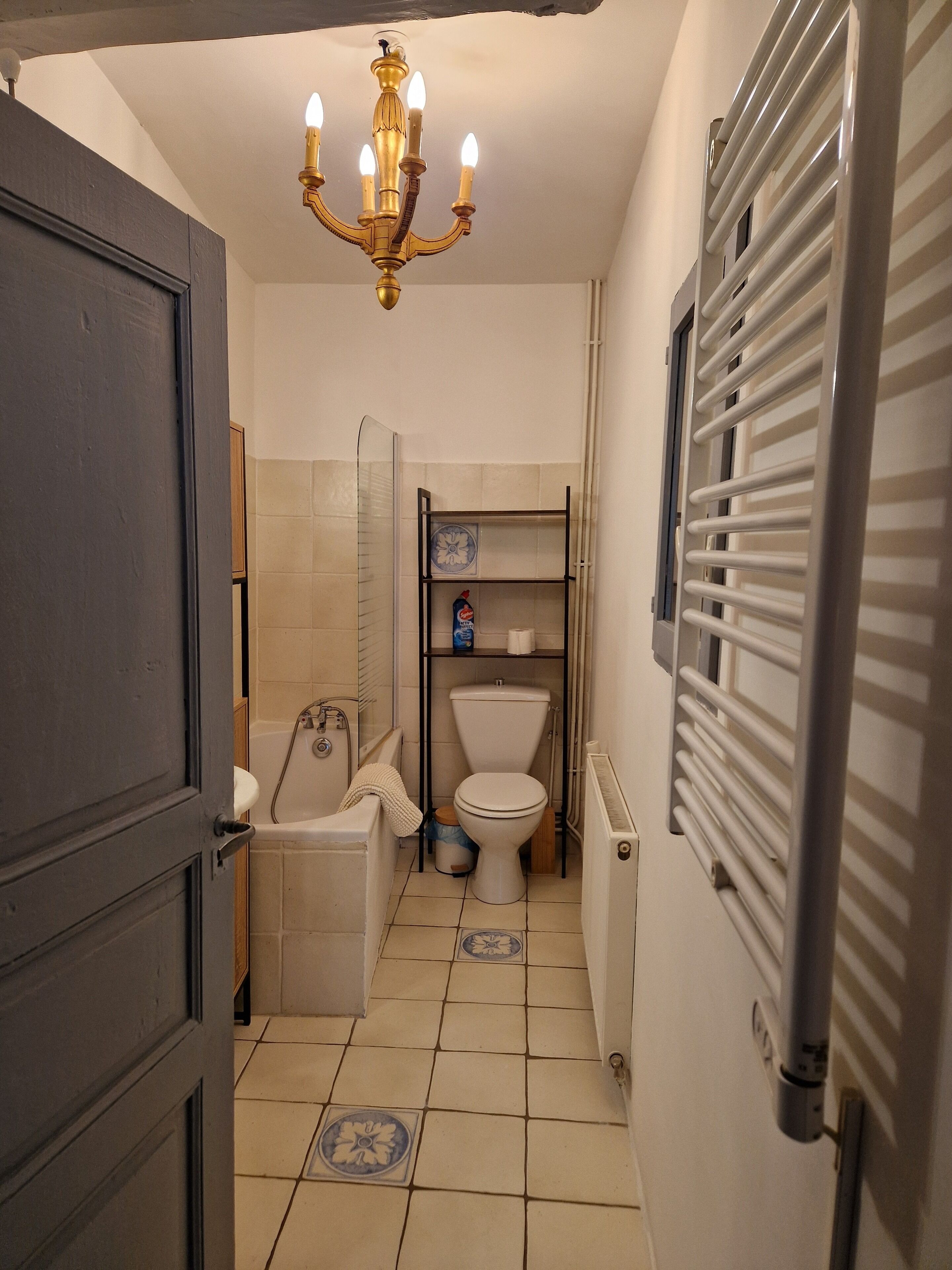 A compact bathroom with a toilet, sink, and bathtub. A chandelier hangs from the ceiling, and there is a radiator on the wall.