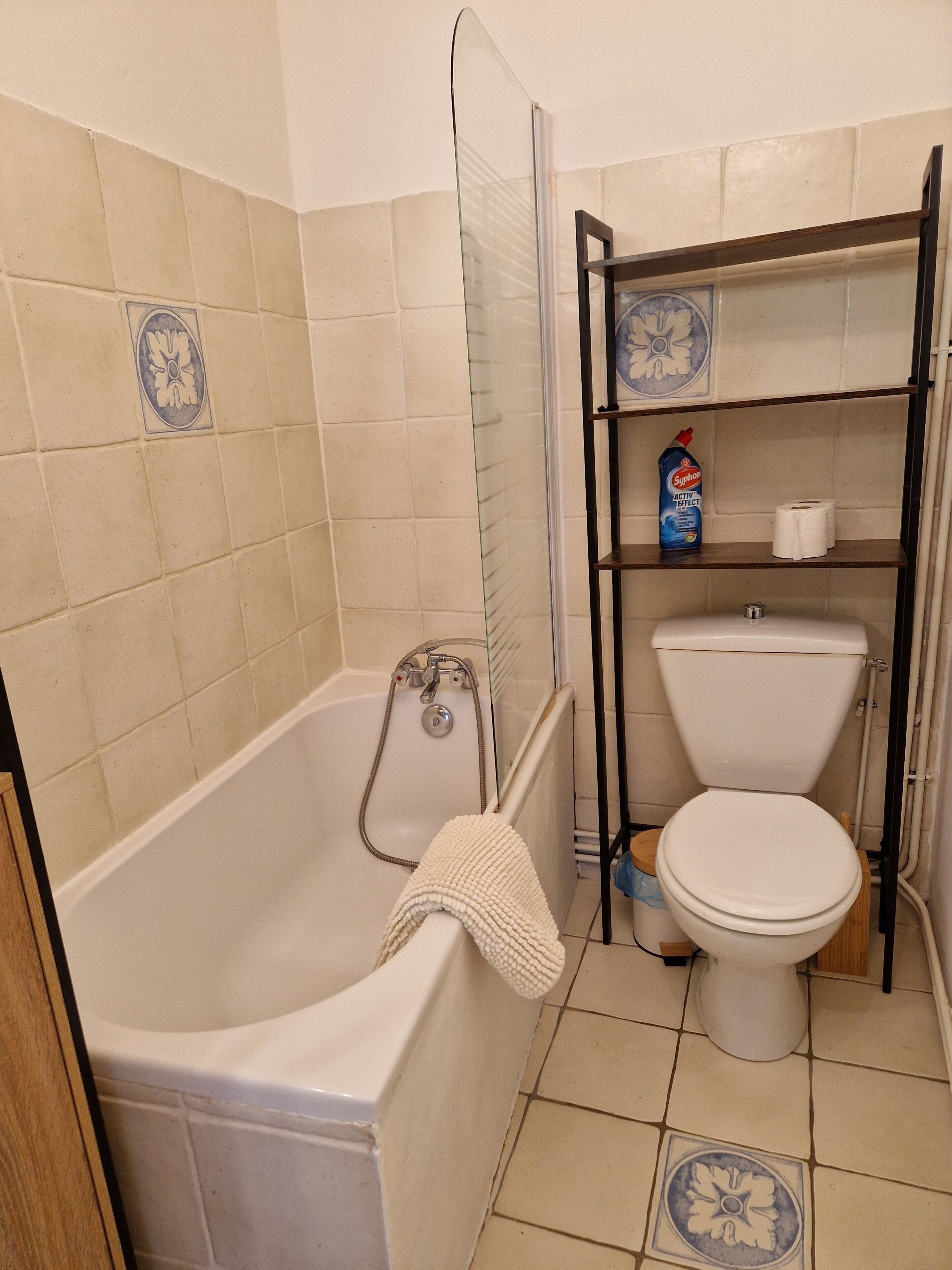 A bathroom with a bathtub, toilet, and a shelf with a bottle of toilet paper and a cleaning product.