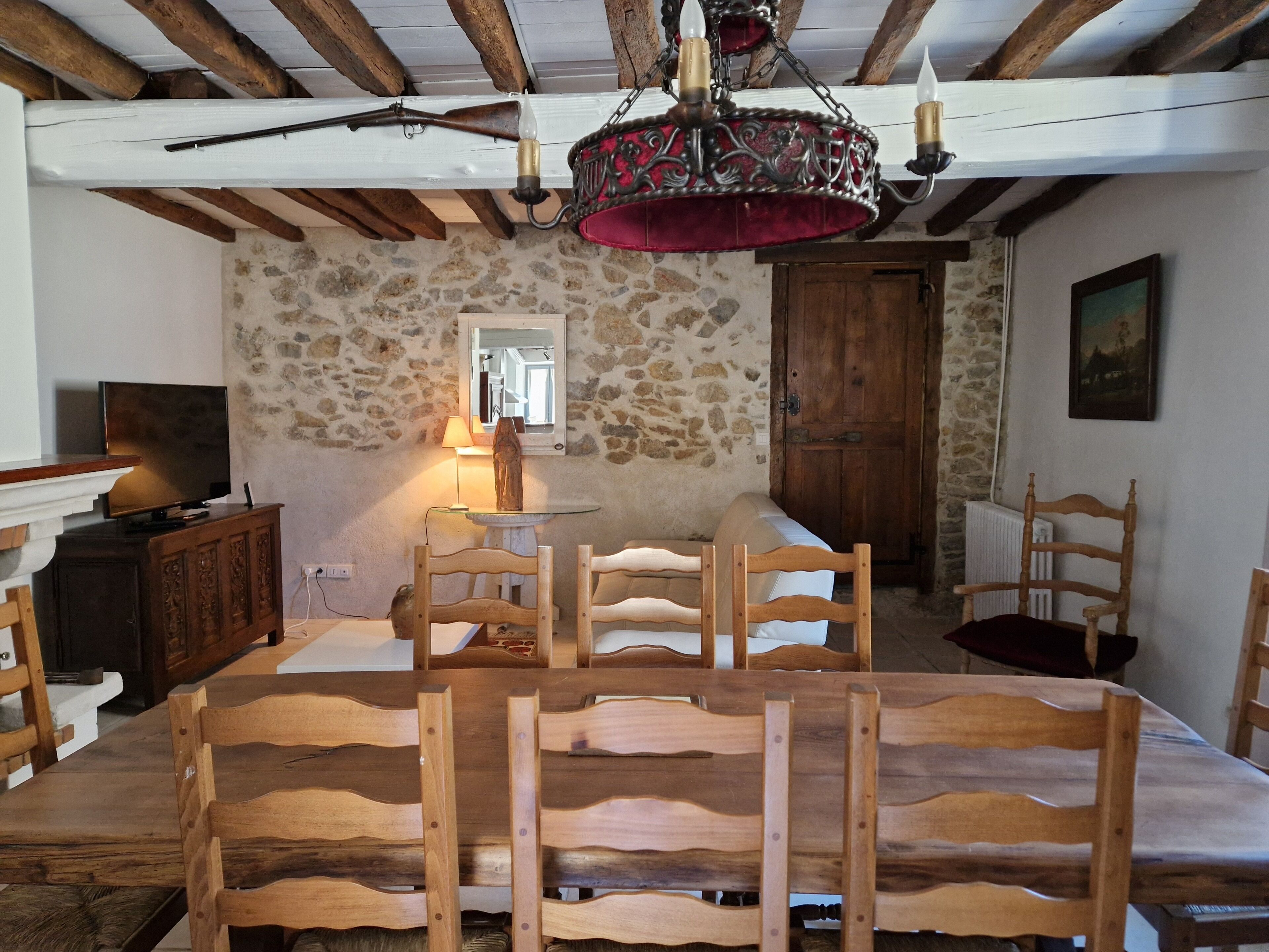 A rustic dining room with a stone wall, wooden furniture, and a chandelier.
