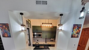 A kitchen with a central island, four stools, and pendant lighting. - The Carriage House of Mount Vernon (Baltimore)