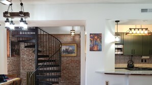 A modern kitchen with a bar area, wooden flooring, and a staircase leading to an upper level. - The Carriage House of Mount Vernon (Baltimore)