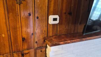 A wooden wall with a decorative emblem, a white brick fireplace, and a thermostat.