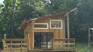 A wooden cabin with a deck, large windows, and a staircase leading to the entrance.