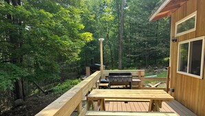 A wooden deck with a grill and picnic table, surrounded by a forest.