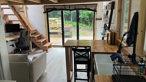 A compact kitchen with a dining table, a single chair, and a built-in oven. A staircase leads to an outdoor area with a view of greenery.