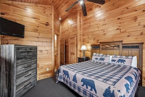 Une chambre dans une cabane en bois, comprenant un lit, une commode, un ventilateur de plafond et un téléviseur fixé au mur.
