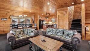 A log cabin interior with a sofa set, a dining table, a kitchen area, and a staircase. - Family Friendly Retreat w/ Hot Tub & Game Area (Gatlinburg)