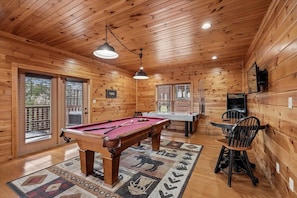 Un intérieur en bois avec une table de billard, des chaises et un téléviseur.