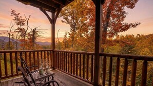 A wooden deck with a railing, a table with chairs, and a view of trees and mountains. - Family Friendly Retreat w/ Hot Tub & Game Area (Gatlinburg)