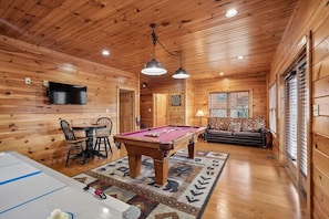 Un intérieur en bois avec une table de billard, un canapé et un téléviseur.