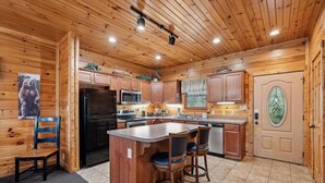 A wooden cabin interior with a kitchen, bar area, and a door with a decorative glass panel. - Family Friendly Retreat w/ Hot Tub & Game Area (Gatlinburg)