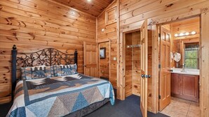 A wooden cabin bedroom with a bed, a wooden door leading to a bathroom, and a window. - Family Friendly Retreat w/ Hot Tub & Game Area (Gatlinburg)