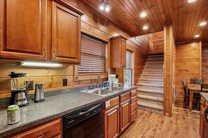 A kitchen with wooden cabinets, a granite countertop, a dishwasher, and a coffee maker. - Scenic Resort Cabin w/ Game Area & Views (Gatlinburg)