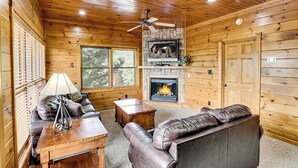Un intérieur de chalet chaleureux avec des murs en bois, une cheminée, des canapés en cuir et un ventilateur de plafond.