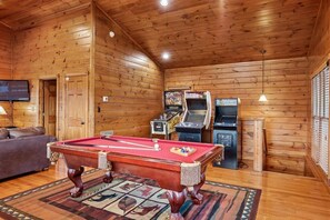Una sala con paneles de madera, mesa de billar, sofá y juegos de arcade.
