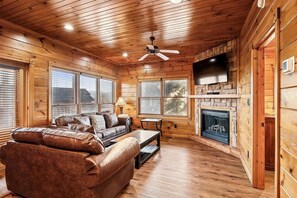 Ein Interieur einer Blockhütte mit Kamin, Deckenventilator und Wandfernseher.