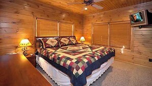Une chambre à coucher dans un chalet en bois, avec un lit, deux lampes de chevet, un ventilateur de plafond et un téléviseur fixé au mur.