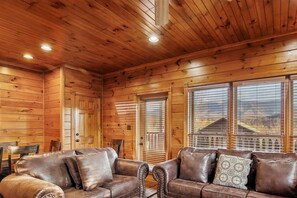 Ein Interieur einer Holzhütte mit einem Ledersofa, einer Tür und Fenstern mit Jalousien.