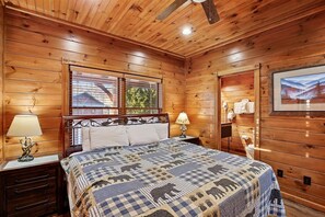 A wooden cabin bedroom with a bed, nightstands, a ceiling fan, and a window with blinds. - Scenic Resort Cabin w/ Game Area & Views (Gatlinburg)