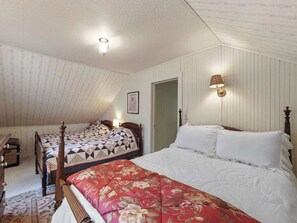 A bedroom with two beds, a sloped ceiling, a door, and a wall-mounted light fixture. - Seven Sisters On Little Glen (Empire)