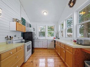 A kitchen with wooden cabinets, a stove, a refrigerator, and a window overlooking greenery. - Seven Sisters On Little Glen (Empire)