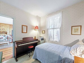 A bedroom with a bed, a piano, a desk, a chair, and a window with curtains.