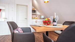 A dining area with a wooden table, black chairs, a bottle of wine, and a fruit arrangement. - Zum Brandenburger Tor 17 (Damme)