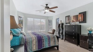 Une chambre à coucher comprenant un lit, un ventilateur de plafond, une commode et un bureau.