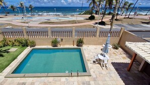 A swimming pool with a view of the ocean, surrounded by a fence and palm trees.