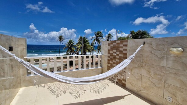 A hammock in a tiled outdoor area with a view of the ocean and palm trees.