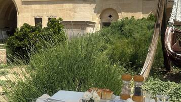 Mesa de comedor al aire libre con comida y bebidas, frente a un edificio con ventanas de arco y fachada de piedra.