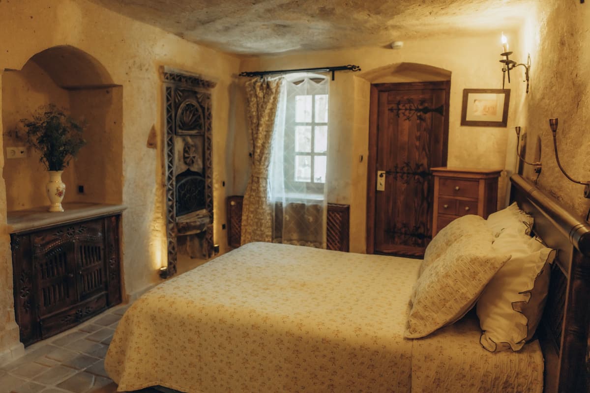 A bedroom with a bed, a wooden dresser, a door, and a window with curtains.