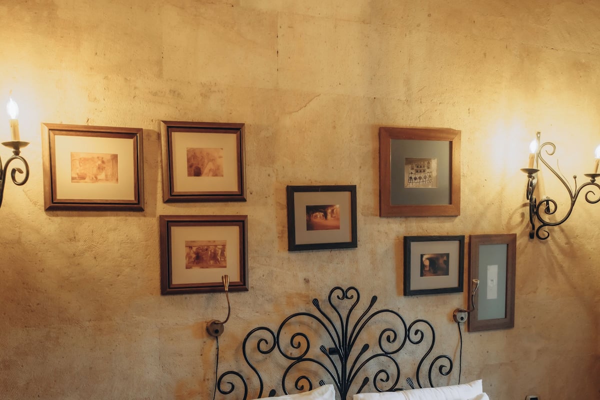 A bedroom with a bed, bedside tables, wall-mounted picture frames, and wall sconces.