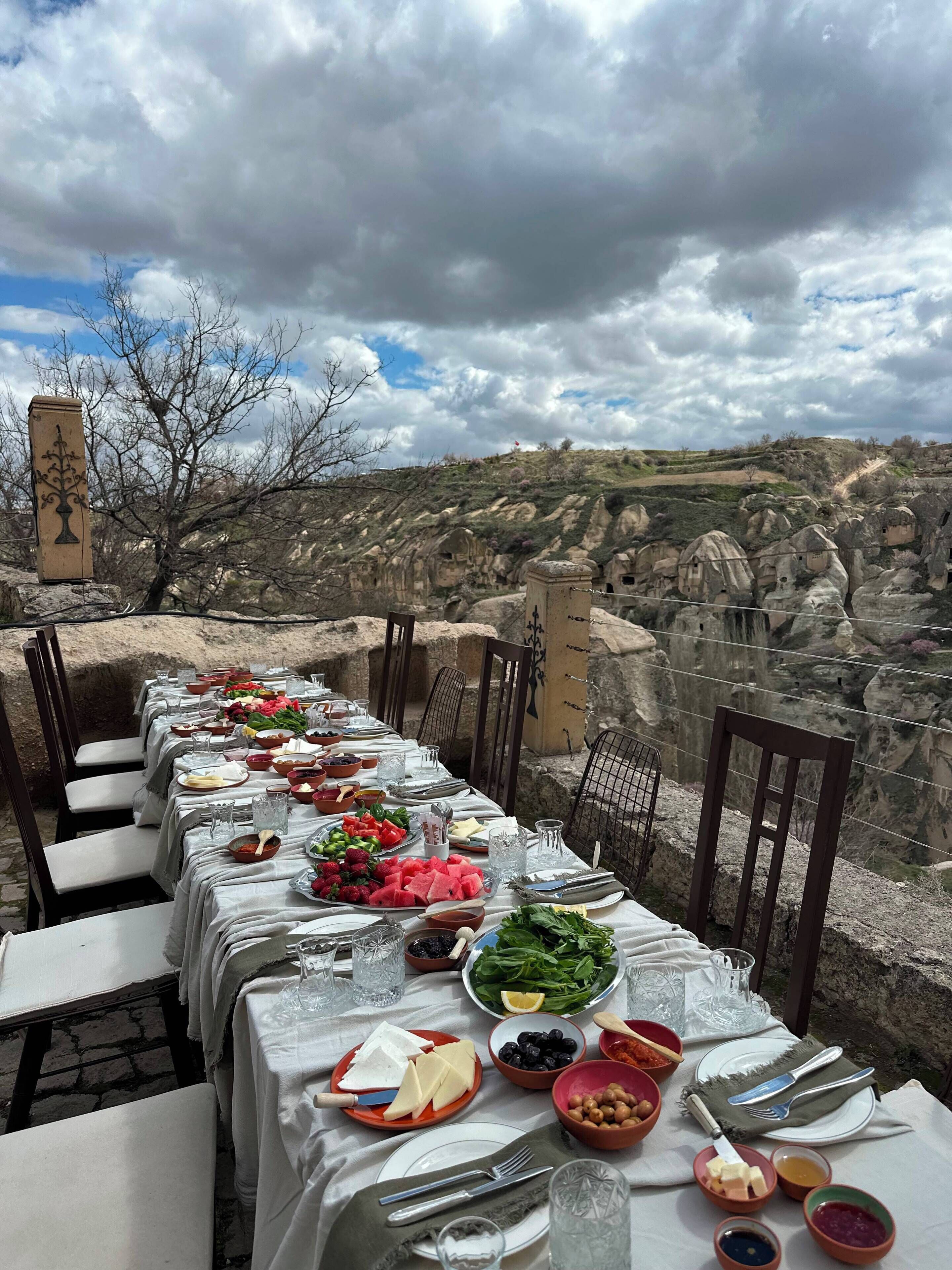 A table set for a meal with a view of a rocky landscape and traditional architecture.