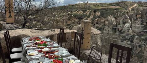 A table set for a meal with a view of a rocky landscape and traditional architecture.